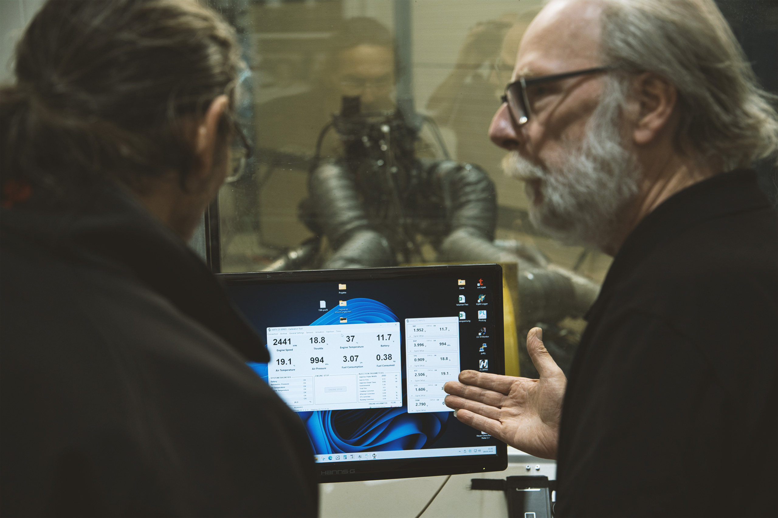 Two aerospace engineers analyzing live diagnostic and performance data from a Hirth engine running on a test bench